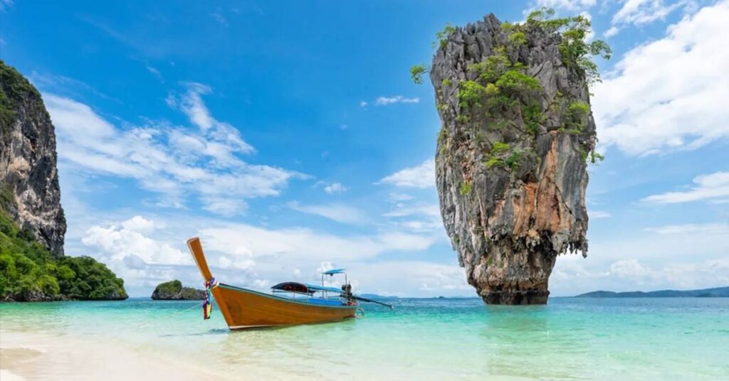 เรือหางยาวกลางทะเลสีฟ้าใส พร้อมภูเขาหินปูนสูงตระหง่านและชายหาดทรายขาว