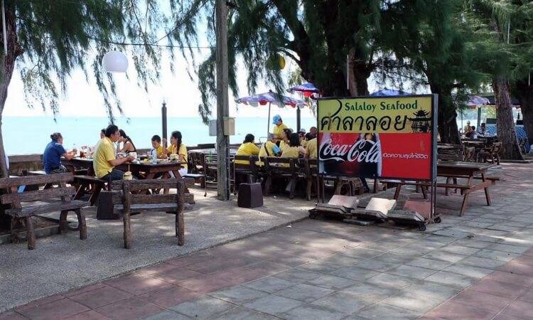 ร้านศาลาลอยซีฟู้ด Salaloy Seafood บรรยากาศริมทะเล มีโต๊ะอาหารใต้ร่มไม้และลูกค้านั่งรับประทานอาหาร